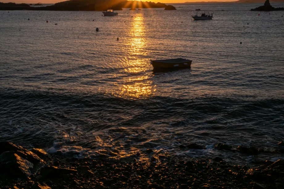 Moored boat at sunrise off Bordeaux Beach, Guernsey, with Herm on the horizon