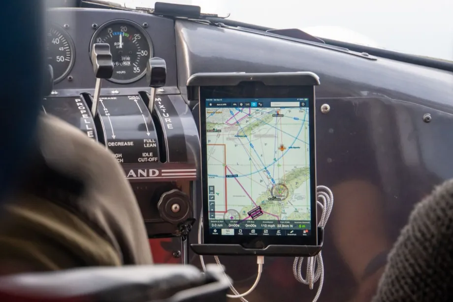 A skipper uses a navigation tablet in the cockpit of a sailboat while planning a passage at sea.